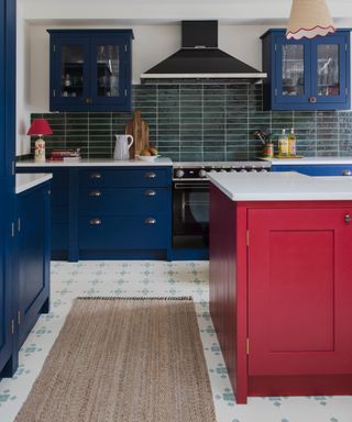 blue and white kitchen with aqua and white floor tiles, rug, red painted kitchen island, white countertops, dark green tiled backsplash