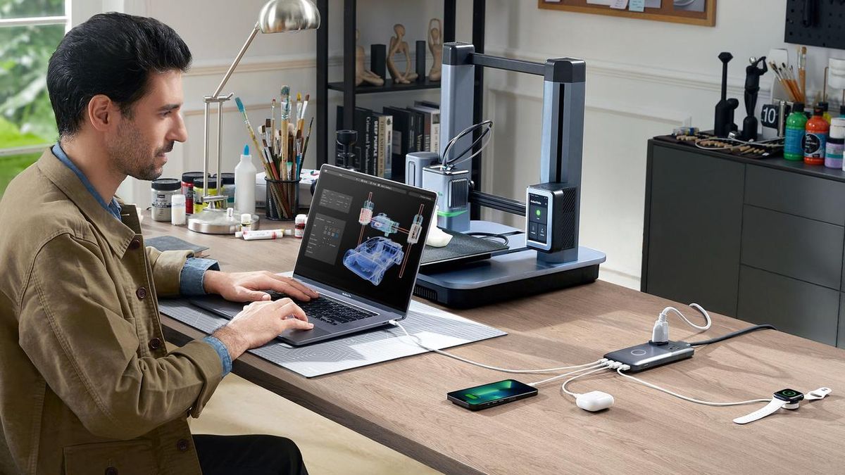 Man sitting at a desk in font of a computer, an Anker power bank charges his laptop and other devices.