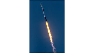 a black-and-white spacex falcon 9 rocket launches into a blue sky.