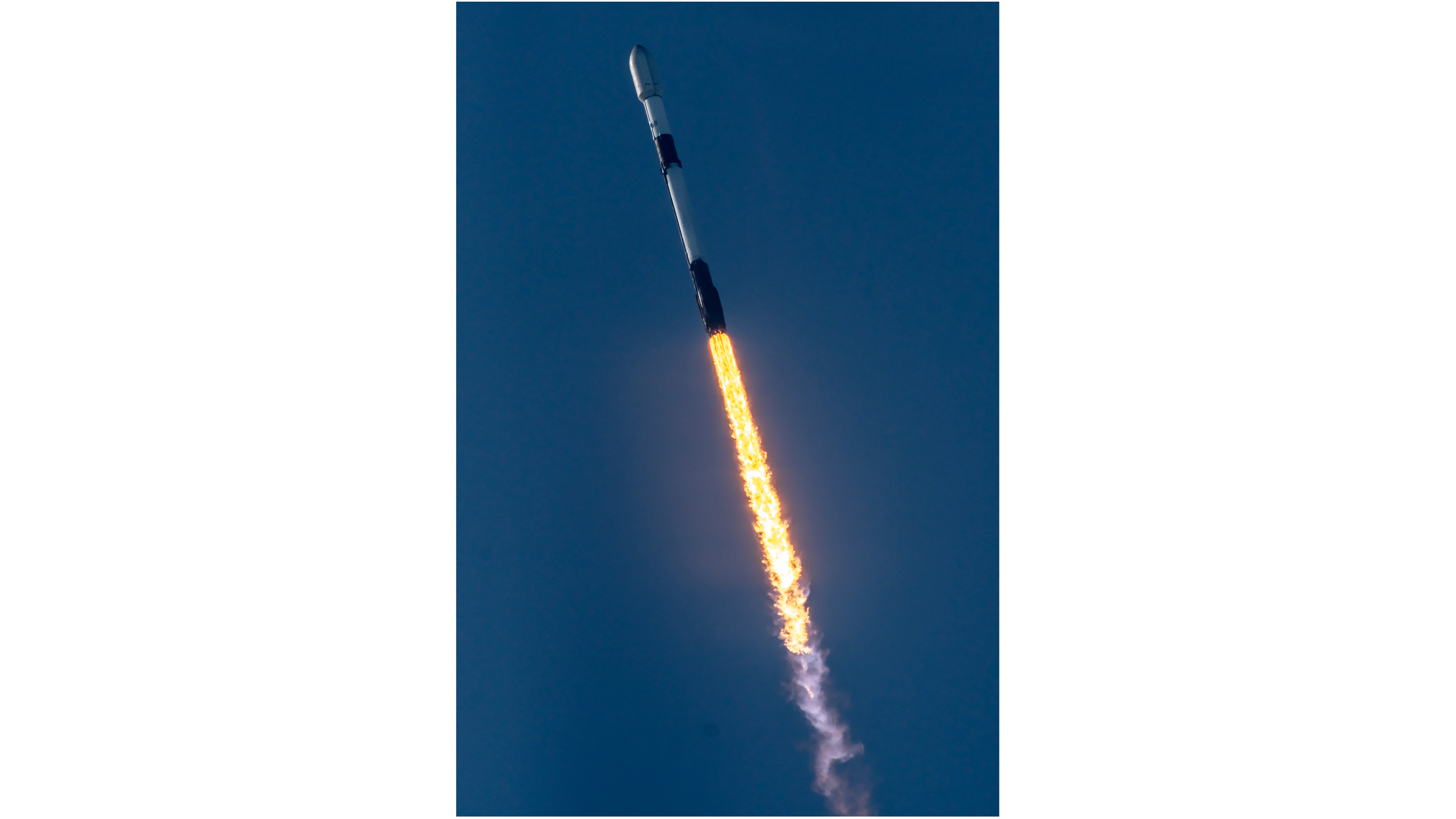 A black and white SpaceX Falcon 9 rocket lifts off into the blue sky.