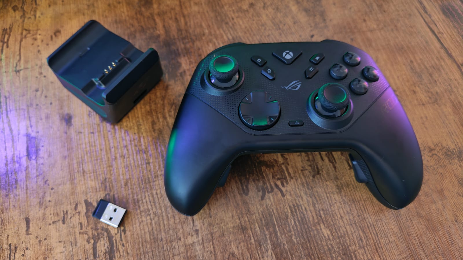 An Asus ROG Raikiri 2 next to its charging stand and USB dongle