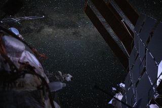 an endless array of scattered stars fills the background while dimly lit components on a space station solar and radiator panels are seen in the foreground.