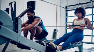 Woman and man row on indoor rowing machine