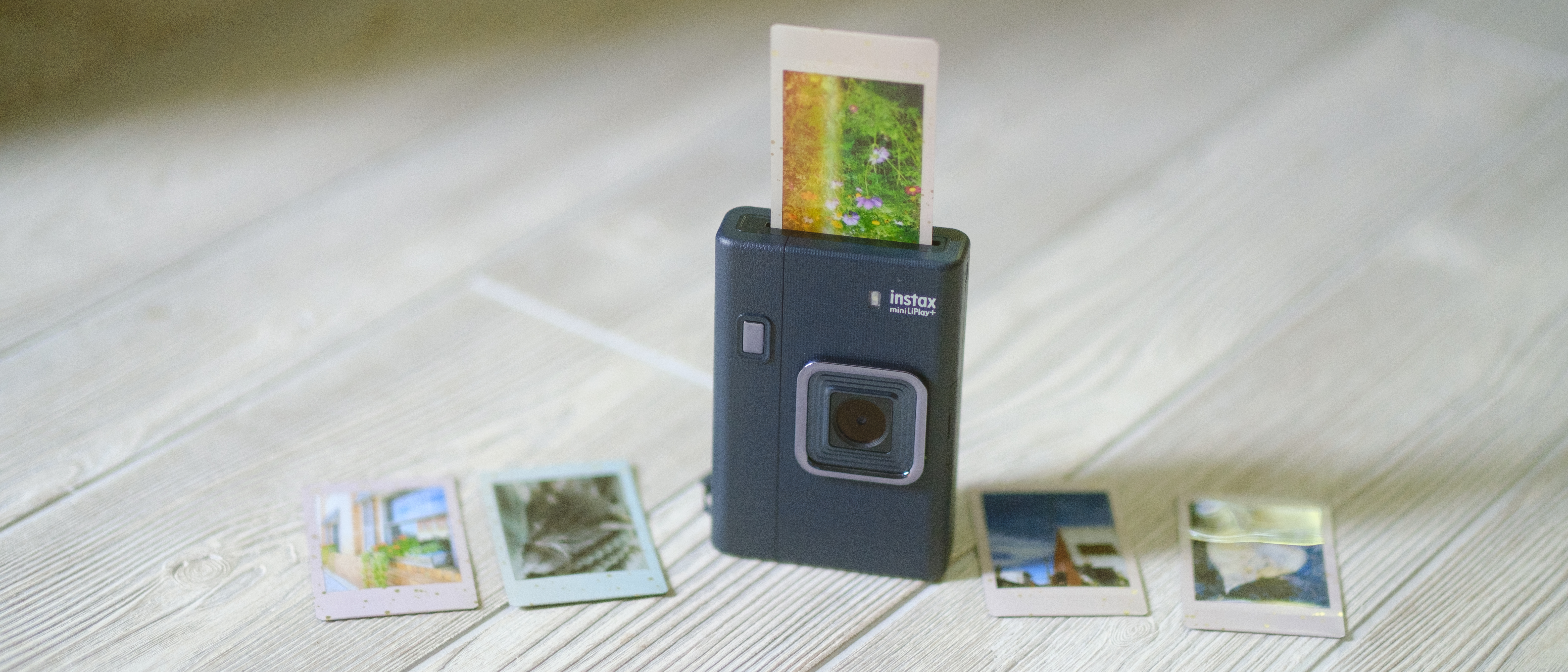 The Fujifilm Instax Mini LiPlay+ on a white wood background with instant film prints