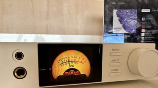 The Topping DX5 II on a light-wood table, showing the VU meter, ports and just-seen remote