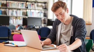 A student in a college library working on a laptop