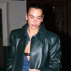 Dua Lipa wearing a long green leather coat, denim jumpsuit, kelly green Chanel 25 bag, and furry brown boots