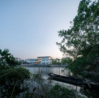 A view of the white three storey school building from across the river.