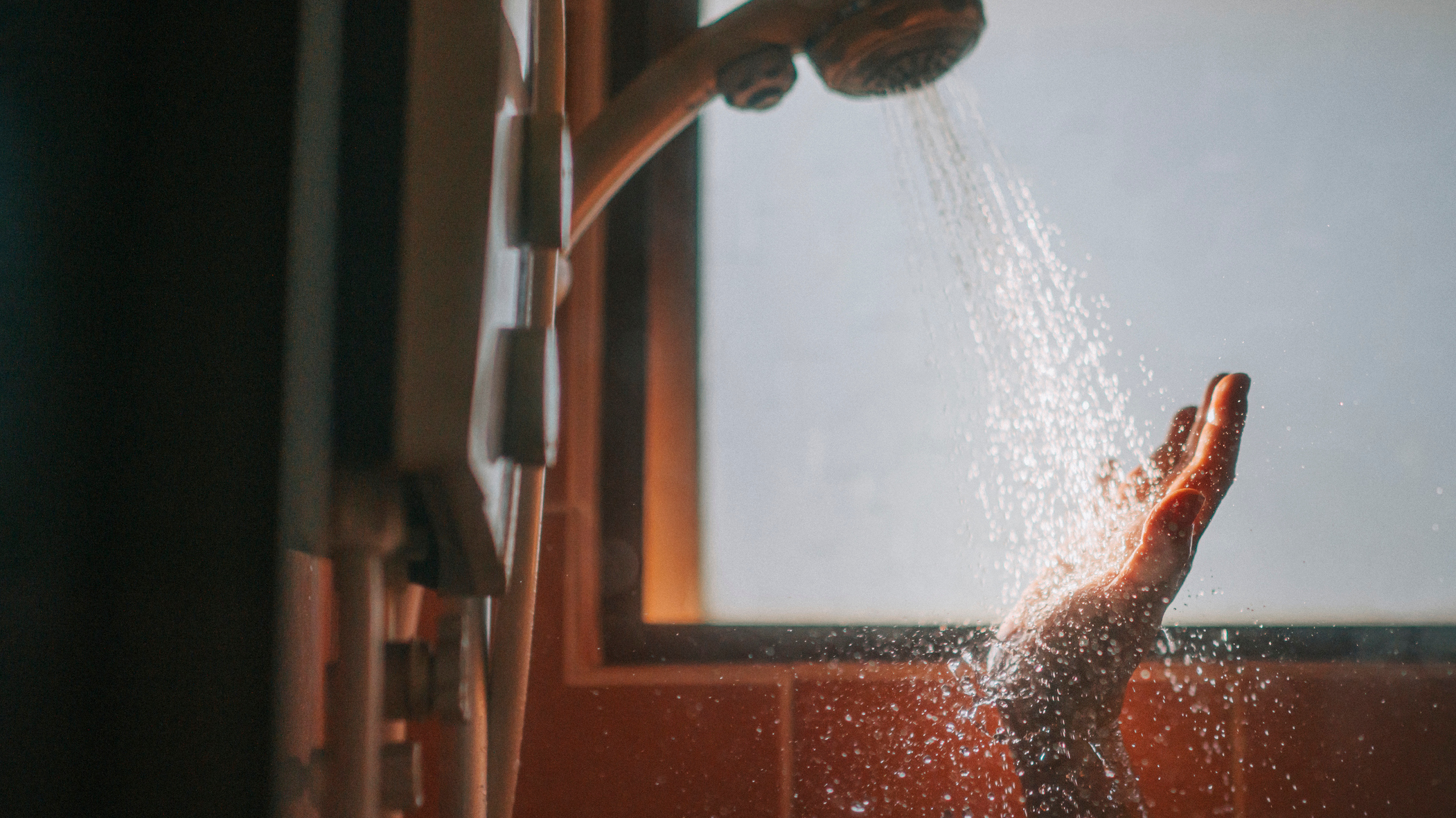 Hand held under shower head, water bouncing off the palm and catching the light