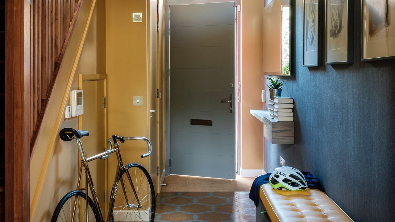 A narrow hallway painted in yellow and black with a storage bench and grey front door