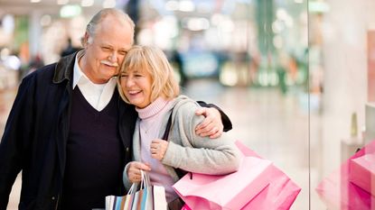A senior couple smiling and carrying colorful shopping bags in a mall 