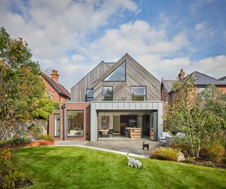 The rear exterior of a detached self build home with pitched roof. There are bifold doors which open fully out into the garden from the kitchen. There is a lawn and a pet dog and cat