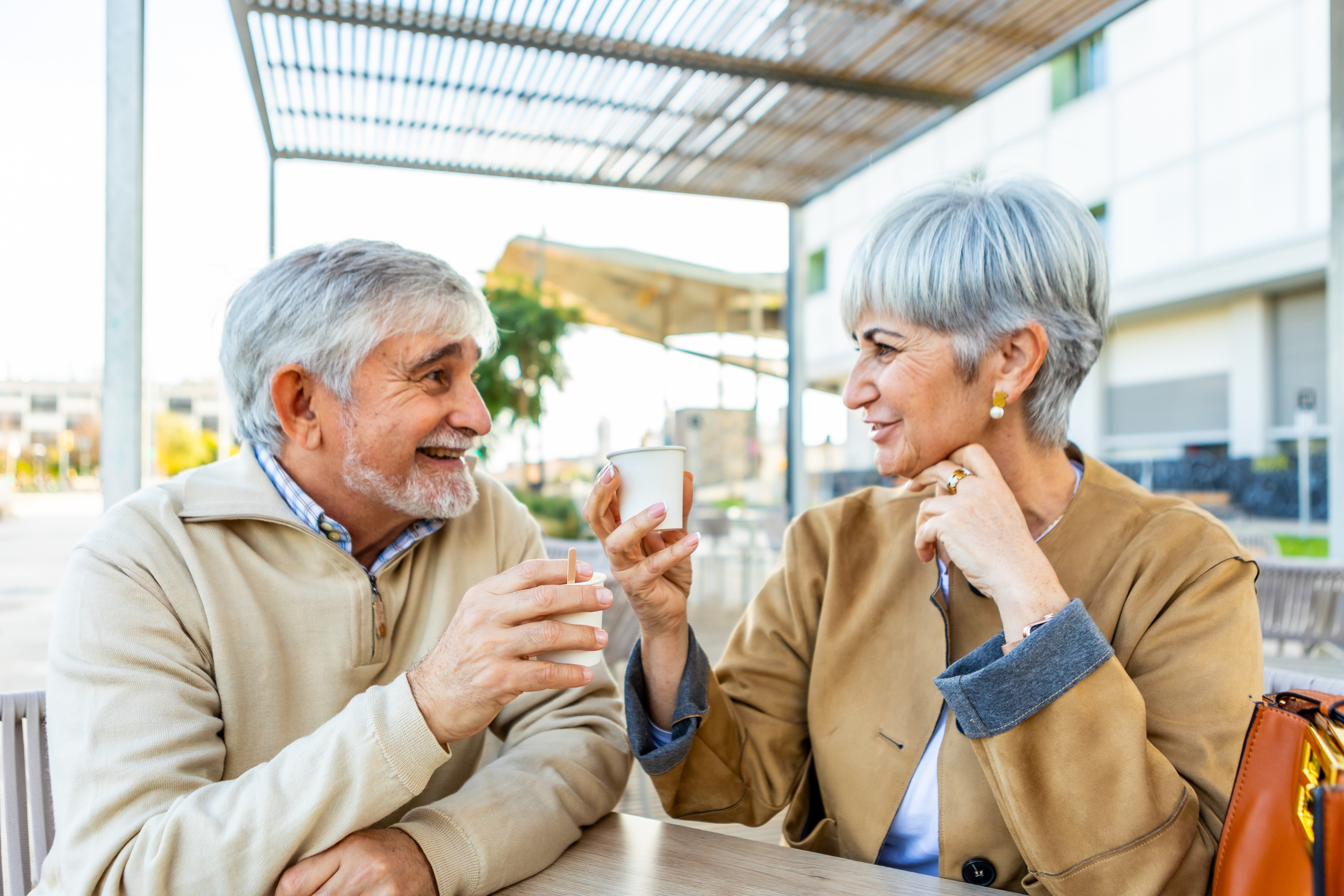 Mature senior couple sitting at an outdoor caf&amp;eacute;, sharing coffee, smiling and chatting in a relaxed daytime moment of togetherness, friendship and joyful retirement leisure