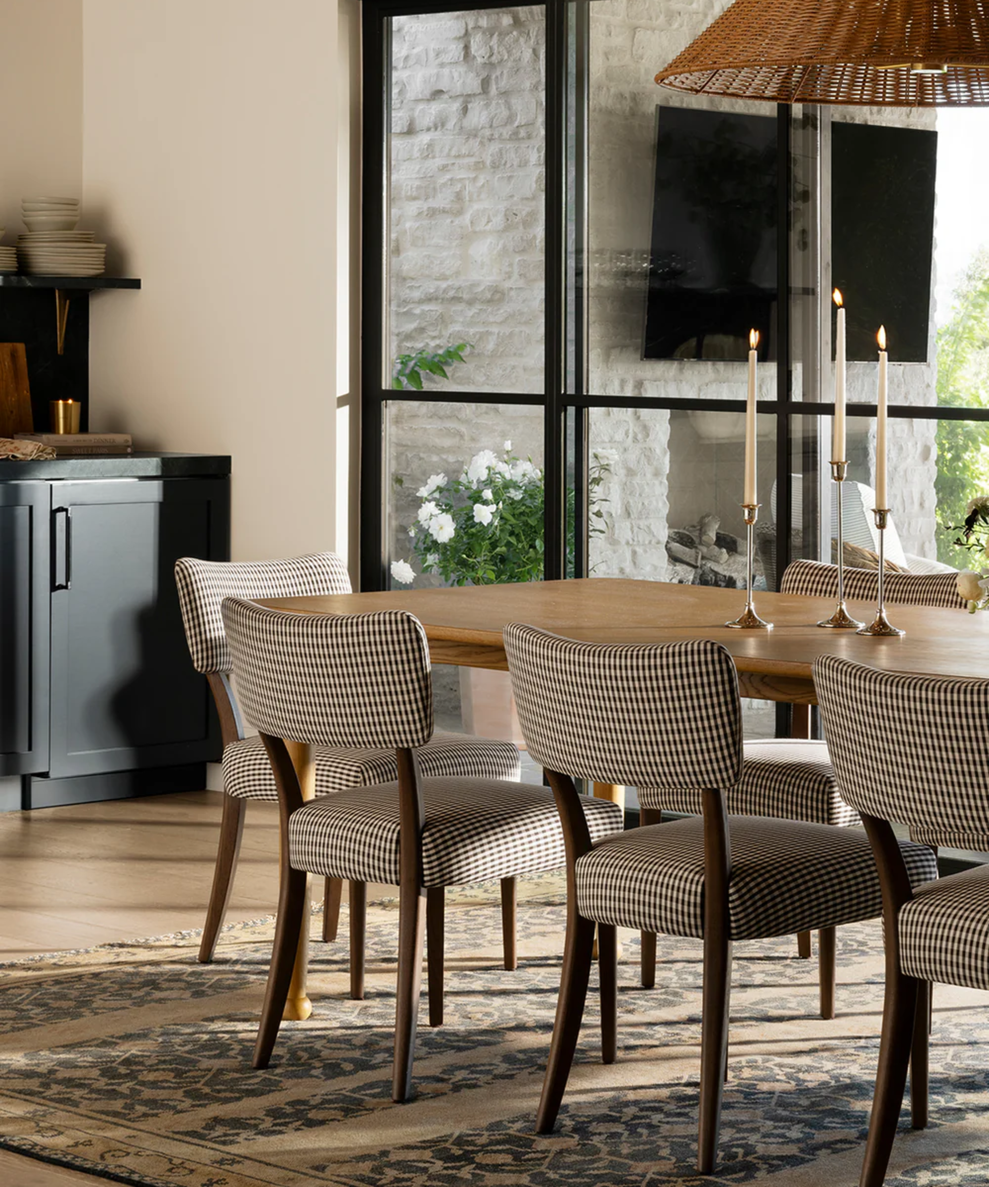 a dining room with plaid dining chairs, a rug on the floor, a large wooden dining table, and silver taper candles
