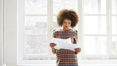 A woman smiles while she looks over paperwork while standing in her home.