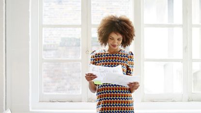 A woman smiles while she looks over paperwork while standing in her home.