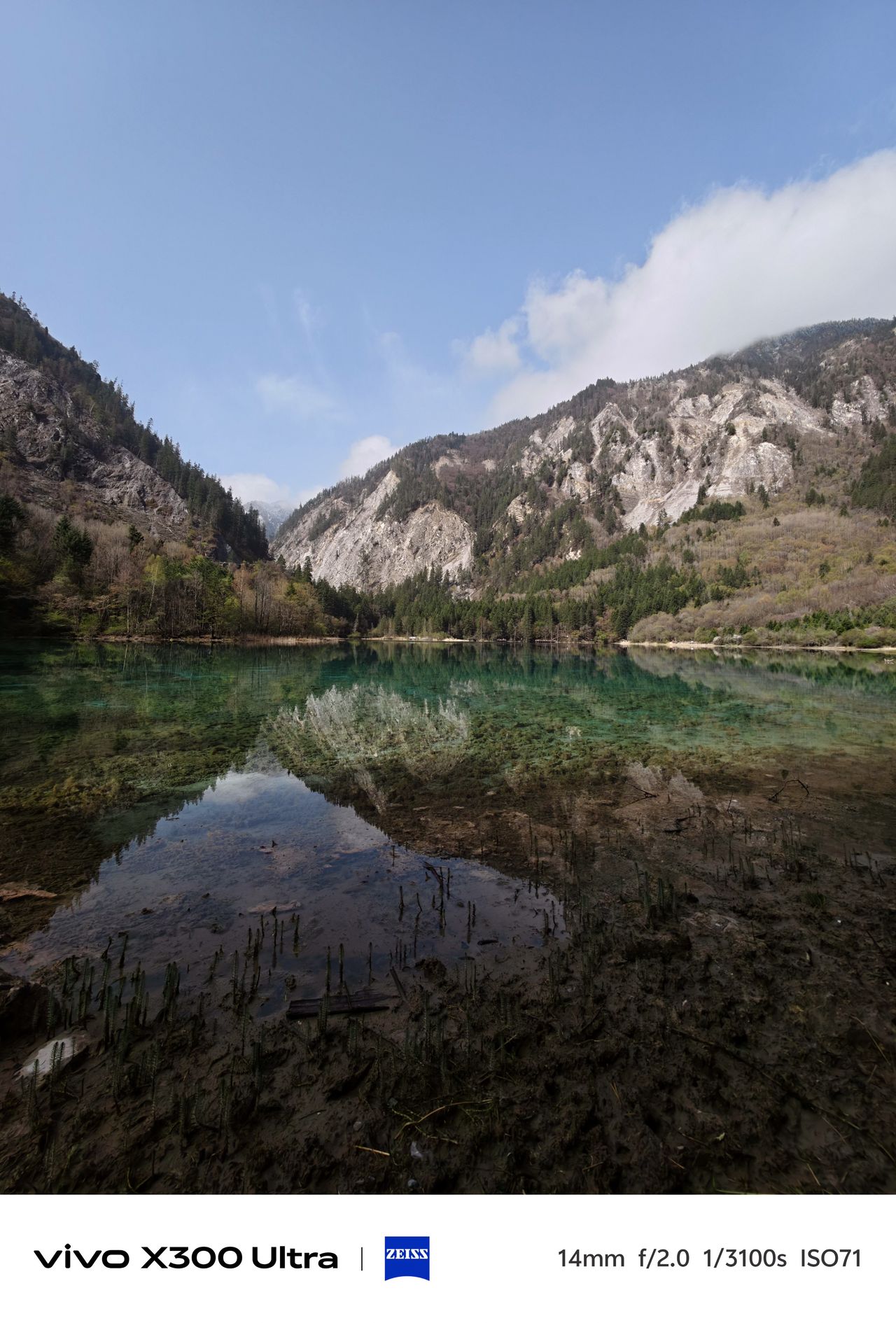 A wide scenic view of a transparent turquoise alpine lake reflecting rocky mountain peaks.