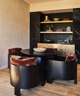 A dark, moody dining table with four curved chairs, and a shelving unit