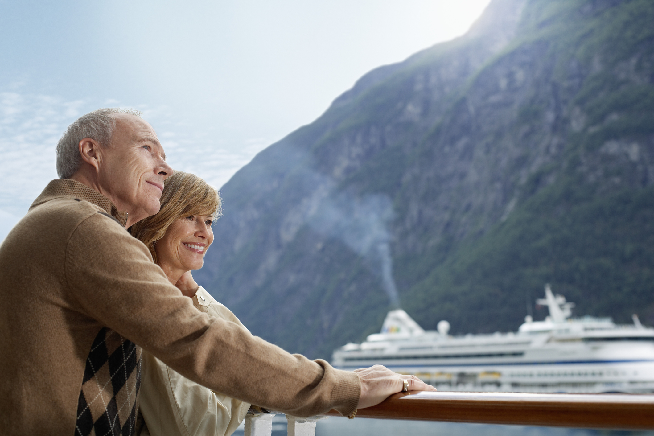 A mature couple on a deck of a cruise ship with another cruise ship in the background.