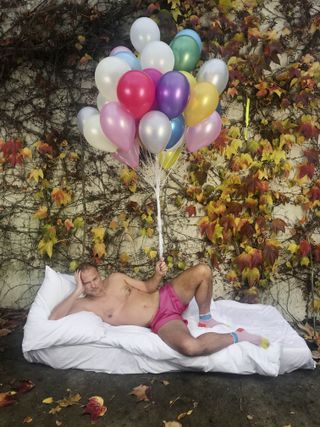 Juergen Teller in self-portrait, lying on mattress outside, with pink shorts and balloons