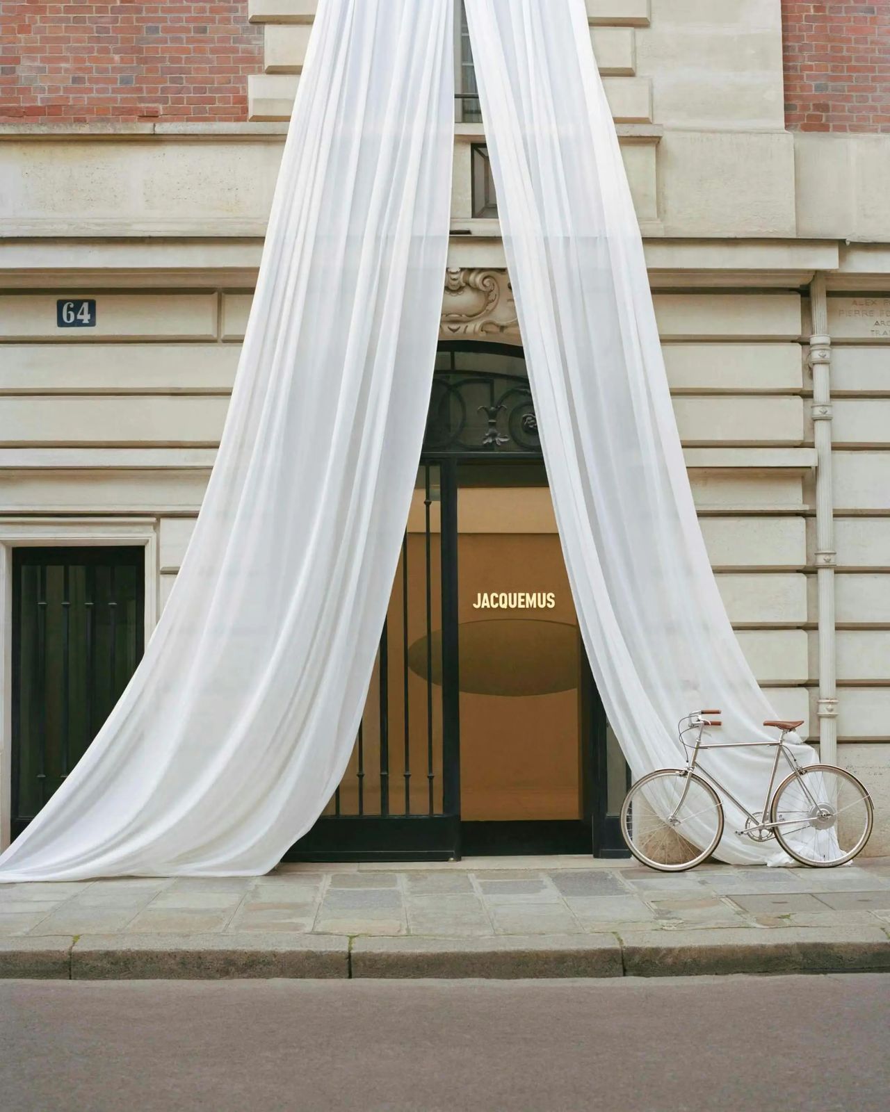 The outside of a fashion store features warm lighting and is decorated with an hanging, monumental white curtain opening up in an A-shaped triangle.