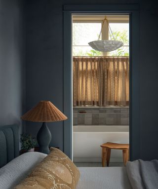 blue bedroom with rattan accessories and view into ensuite with cafe curtain