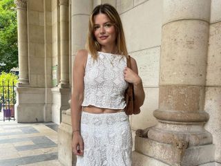 The woman is wearing a white lace sleeveless top and a matching midi skirt.