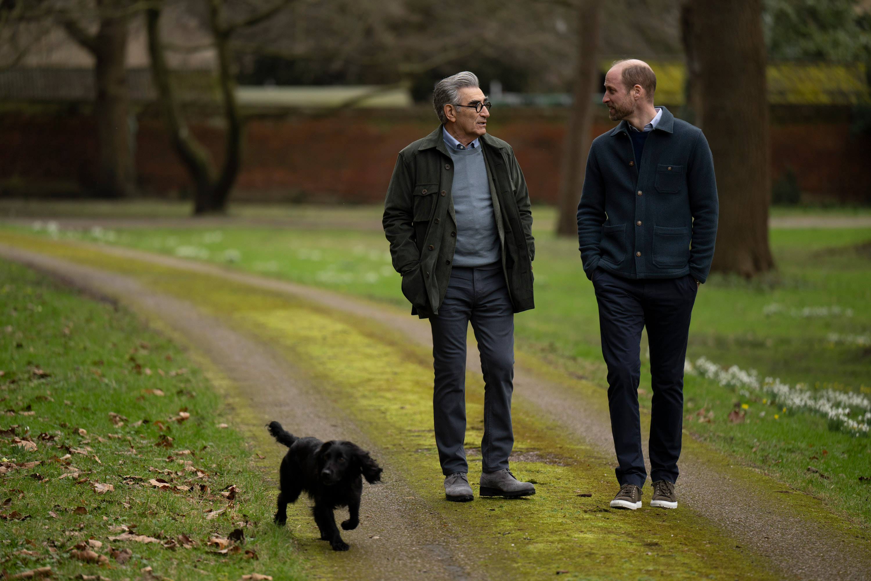 Prince William walking in a park with Eugene Levy and Orla the dog