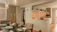 A bright dining room near an open concept kitchen with a fully set dining table with lit candles and pendant lamps.