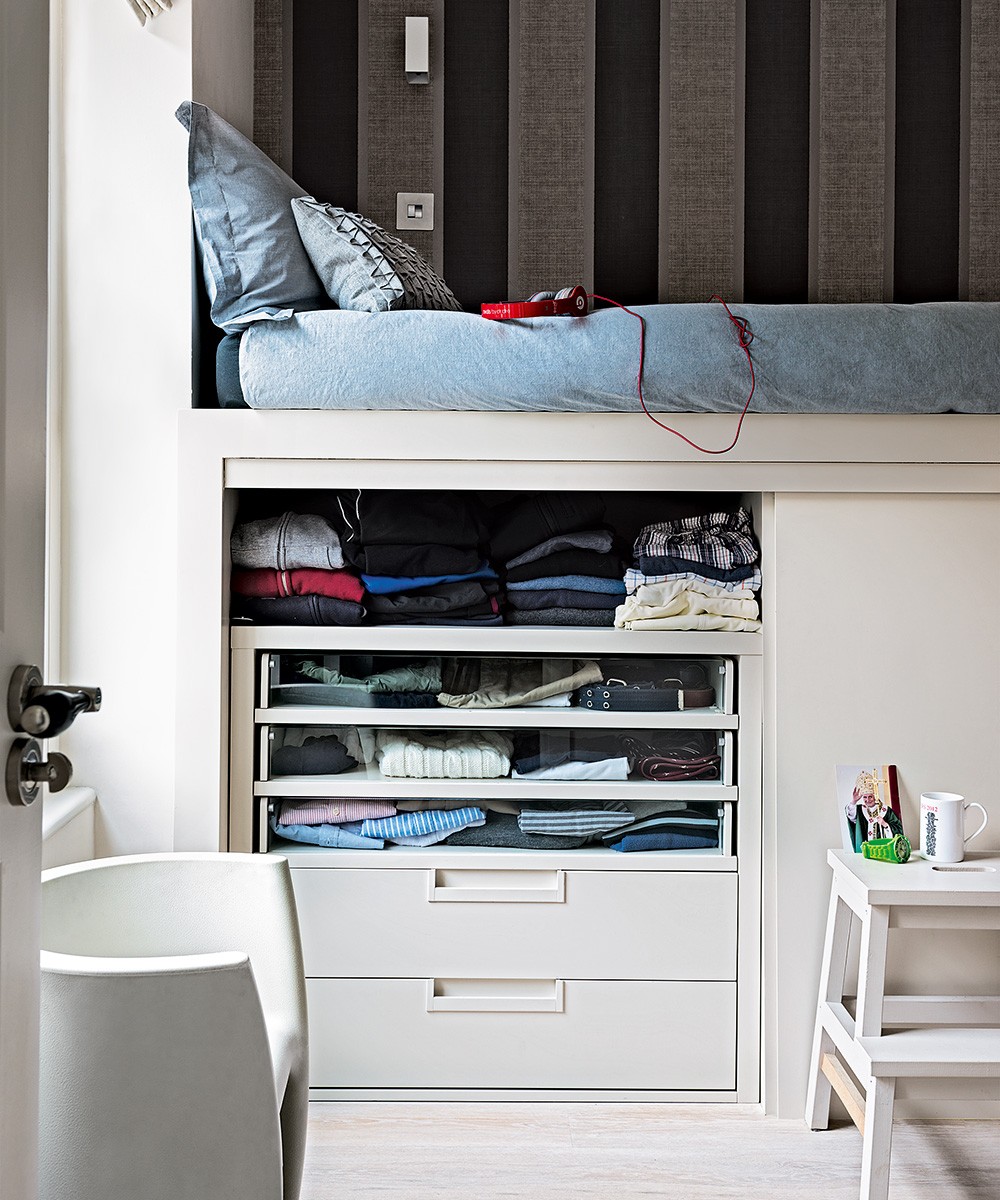 A white raised bed with clothes storage underneath and a wide-striped wallpaper.