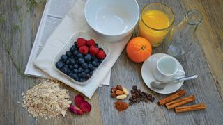 Food ingredients laid out for food photography project: bowl, fruit, cup, oats, glass bottle and orange juice