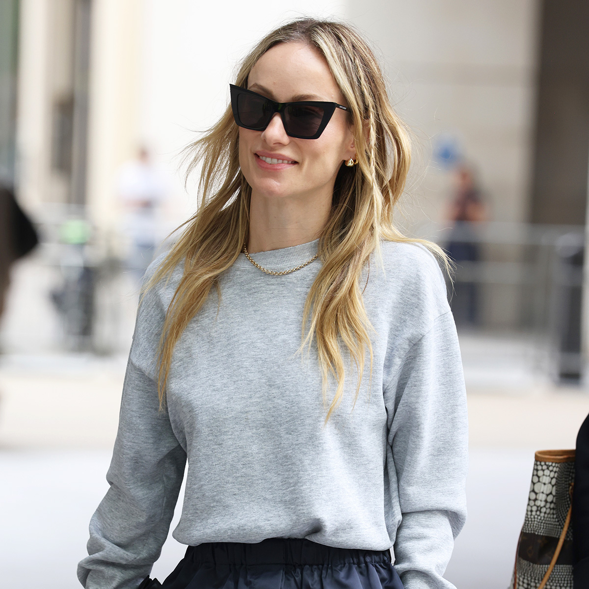 Olivia Wilde wearing a gray sweatshirt, satin knee-length skirt, and ruched loafers in London