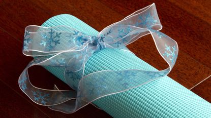 Rolled up yoga mat with ribbon tied around it on wooden floor