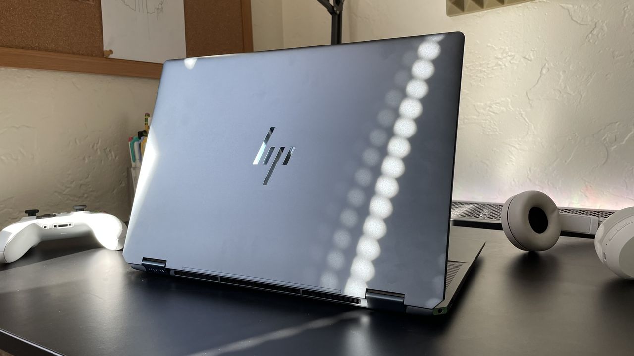 An open, dark gray laptop viewed from the back on top of a black surface against a white background.