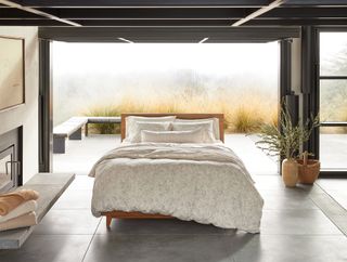 white bedding on a bed that is in the middle of a modern gray room. The back wall is an open window leading out to a foggy landscape