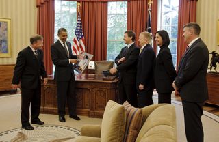 In the Oval Office of the White House, Space shuttle STS-133 mission Commander Steven Lindsey (far left) presents a montage to President Barack Obama as crew members Michael Barratt, Pilot Eric Boe, Nicole Slott, and Stephen Bowen look on, May 9, 2011.