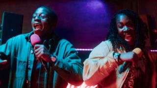 David Jonsson and Vivian Oparah singing karaoke in a colorfully lit room in Rye Lane.