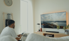 A man watches TV using a Bose Smart Soundbar and the Bose Ultra Open earbuds as his rear channel speakers