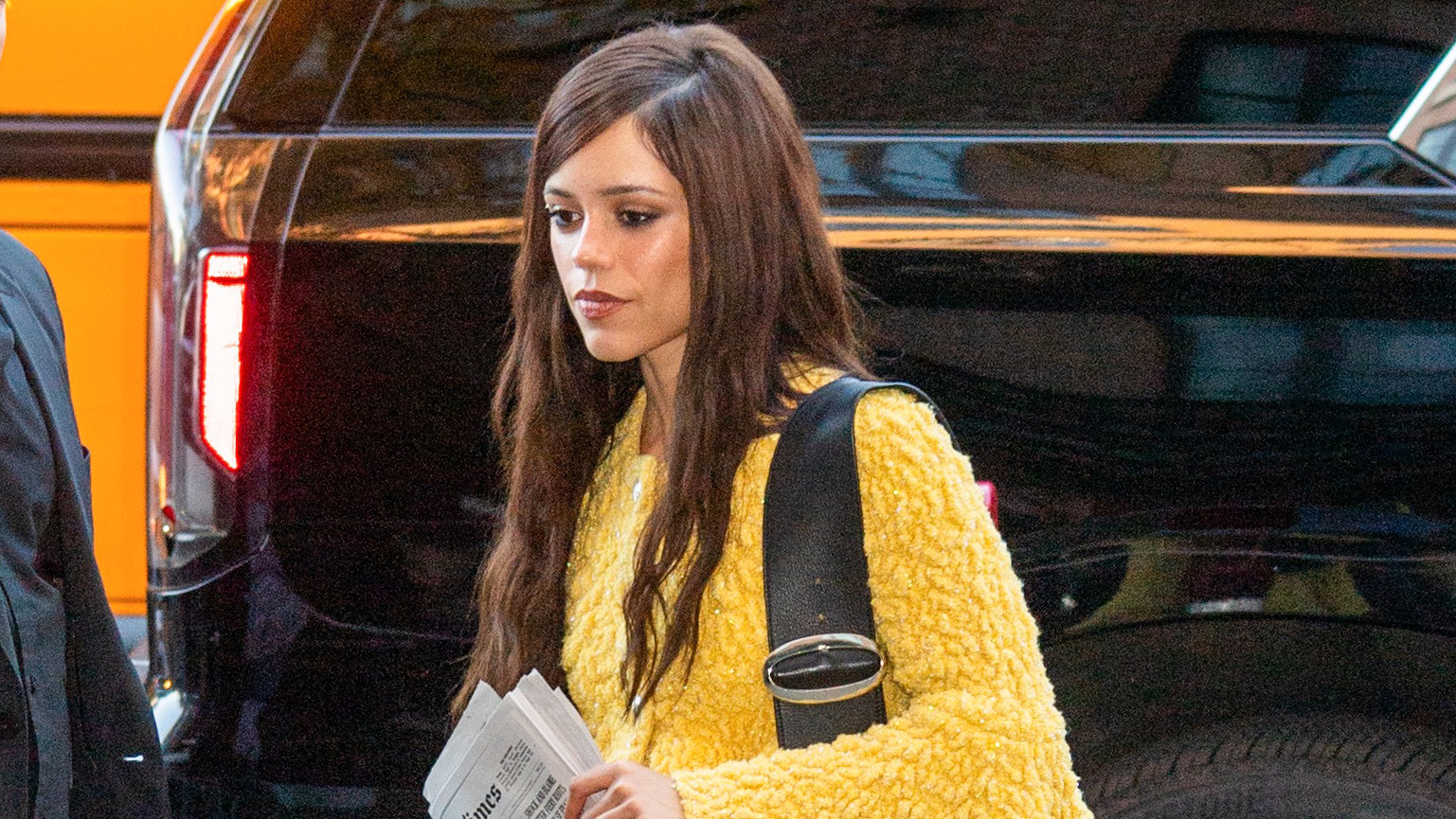 Jenna Ortega wearing jeans, a yellow sweater, and matching yellow pumps.