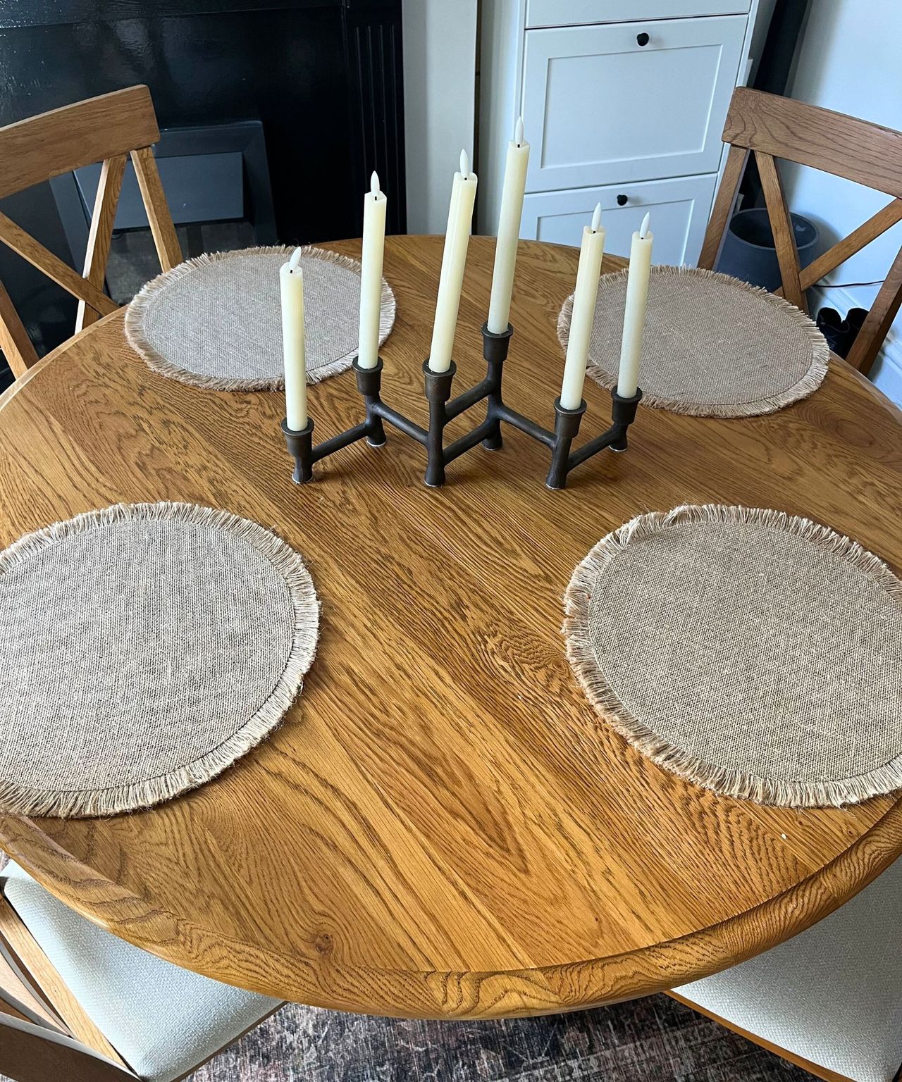 A round wooden dining table with four woven placemats, and a candle holder with LED candles