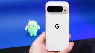Google Pixel 10 Pro XL in Porcelain against a blue background with a green neon Android figurine in the background