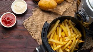 chips cooked in an air fryer, with whole potatoes next to them and two pots of mayonnaise and ketchup