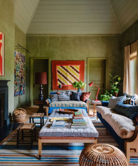 A cozy and eclectic living room with green limewash walls, a sloped ceiling painted light green, a striped rug and colorful decor. 