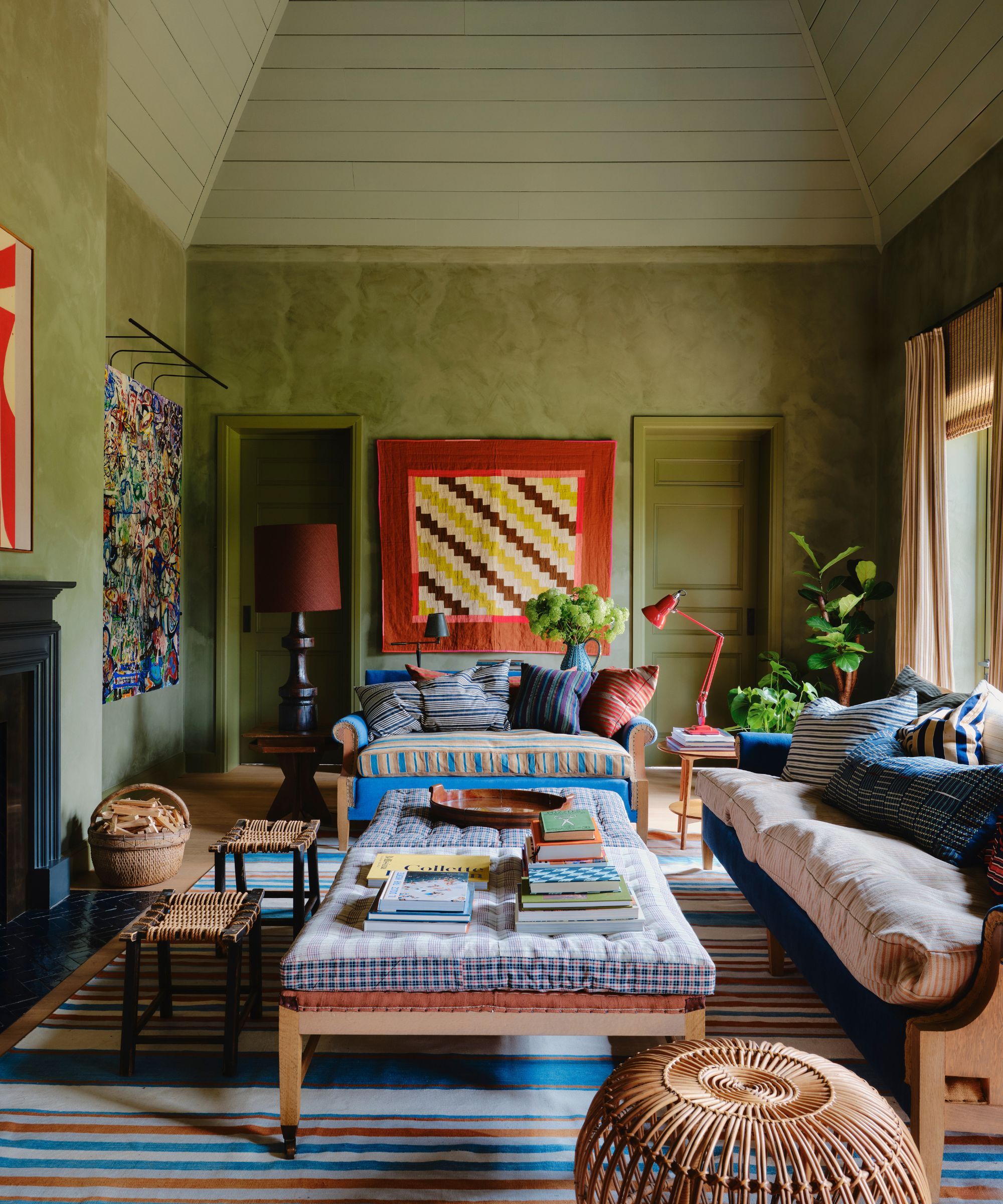 A cozy and eclectic living room with green limewash walls, a sloped ceiling painted light green, a striped rug, and colorful decor.