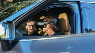 A person is wearing a VR headset whilst sat in a car.