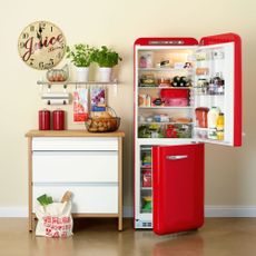 cream wall with red fridge and clock on wall with fruits and drinks
