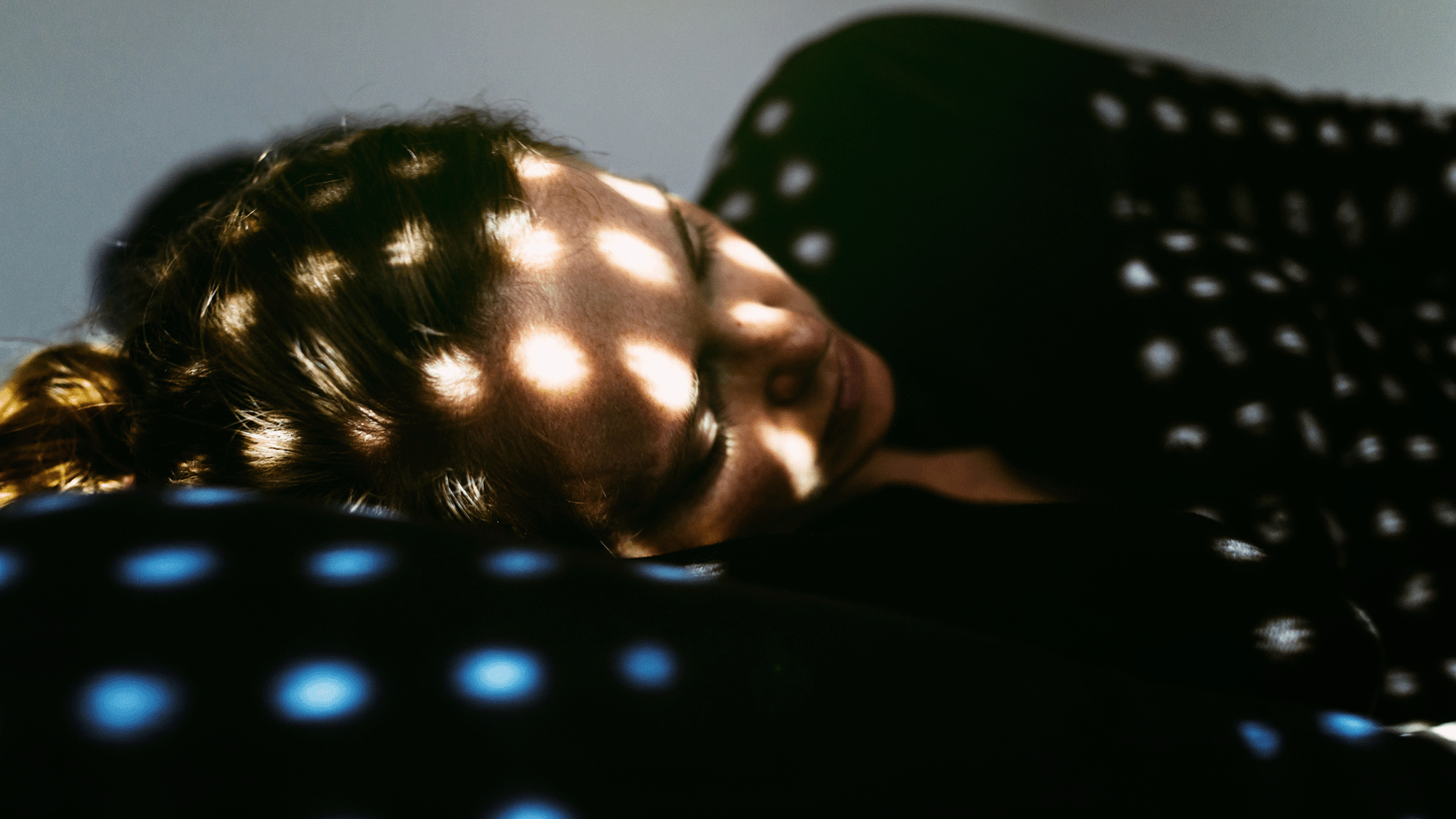 A woman wearing a dark top with her blond hair in a ponytail lays on a blue mattress