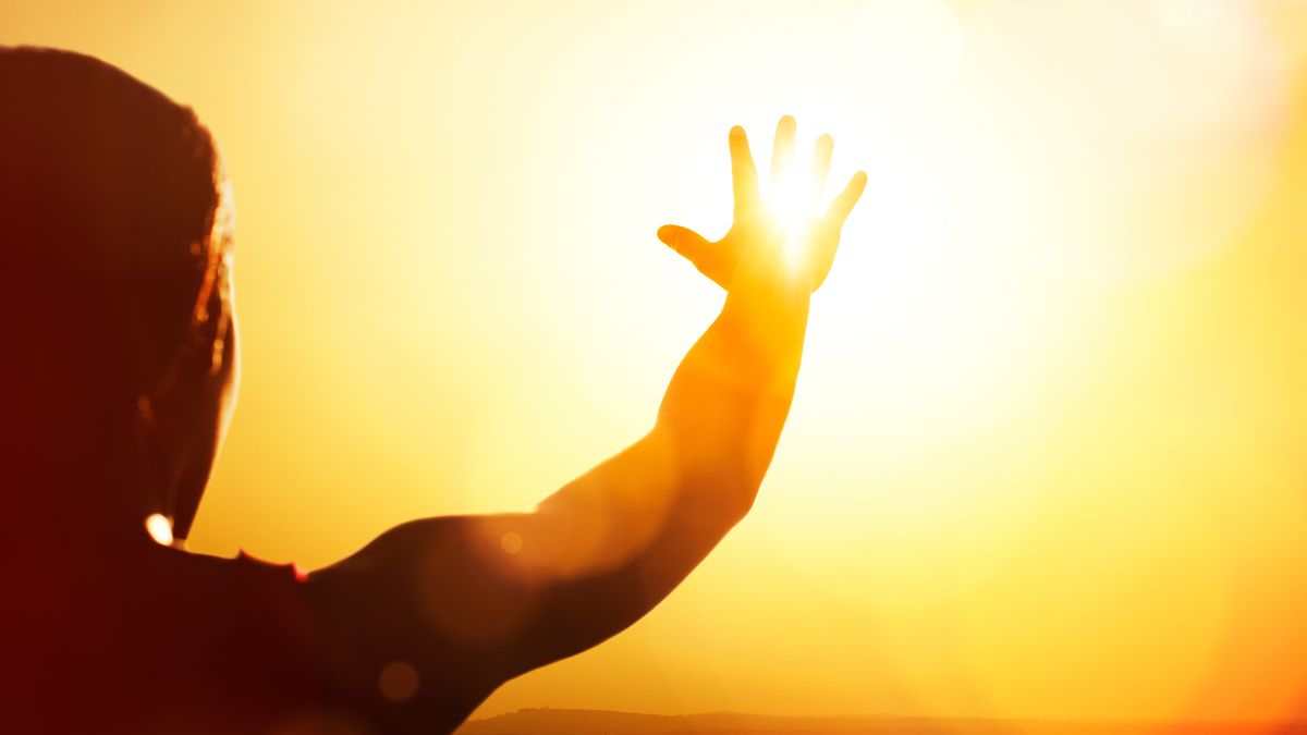 Young woman shown in silhouette as she&#039;s reaching for the sun.