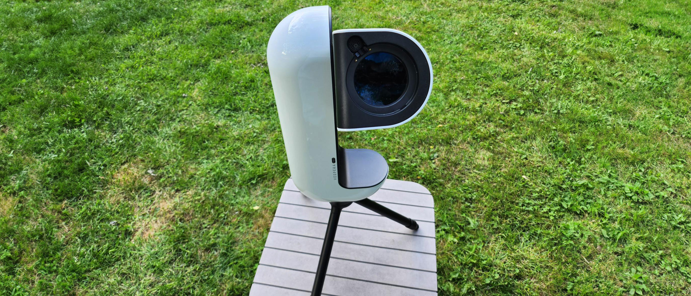 The Vaonis Vespera Pro smart telescope pointing at the sky on a brown table with grass in the background.