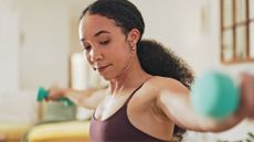 close up shot of a woman lifting two light dumbbells out to her sides in a home setting. 